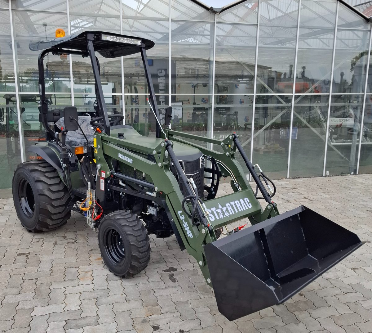 Startrac 26 mit Frontlader, Rundumleuchte und Industriebereifung auf gepflastertem Hof